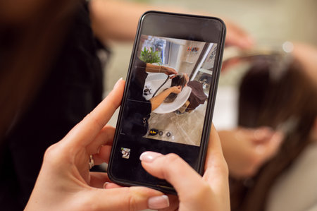 Closeup of manicured hands holding a black smartphone in live view mode and taking a picture of a hair wash in beauty salonの写真素材