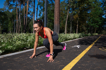 Runner woman on the start position on a running way outdoor. Beautiful park on the background.