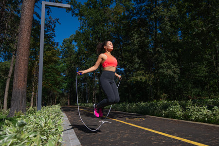 Sporty woman doing skipping workout with jump rope in a park on a sunny day.