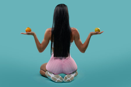 View from the back to a young muscular build fit woman sitting in lotus position and meditating with...