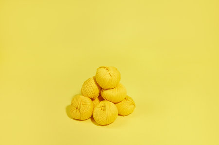 Flat lay composition of pyramid of wool yellow thread isolated on a yellow background. Top view,...