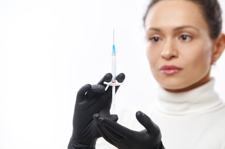 Closeup of hands in black gloves with a syringe isolated on a background of blurred beautiful woman on a white backgroundの写真素材