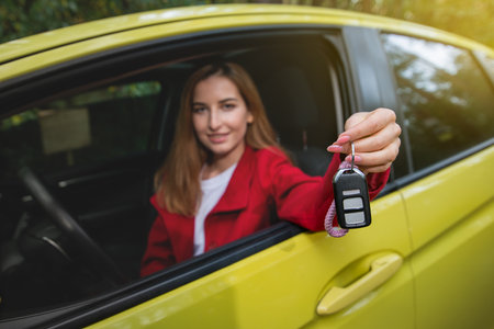 Happy young woman learning to drive car. Young woman holds out the car keys through the driver's seat window. Focus on keysの写真素材