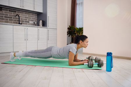 Side view to a sporty woman working out at home and doing plank on an exercise mat. Concept of workout during lockdownの写真素材