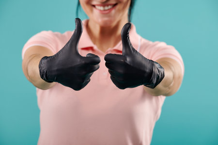 Focus on hands in black latex gloves showing thumbs up. Isolated on a blue backgroundの写真素材