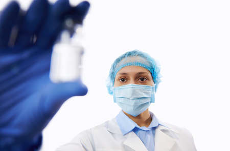 Doctor in protective workwear looking at the vaccine in the hand while showing it to the camera....