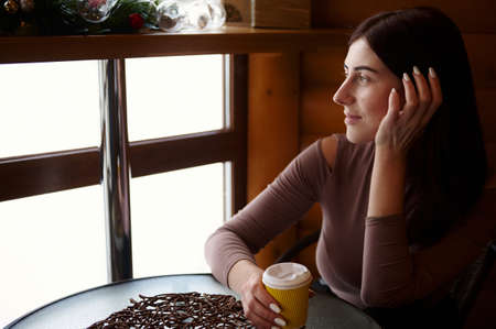Beautiful woman with a cardboard cup of tasty hot drink sitting at the cafe and looking out the...