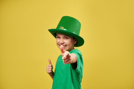 Funny boy pointing finger gun and showing thumb up to camera isolated on yellow background. Saint Patrick's Day. Copy spaceの写真素材