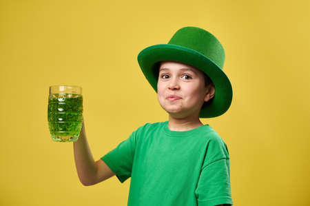 Funny boy in green leprechaun Irish hat with a glass of green drinkの写真素材