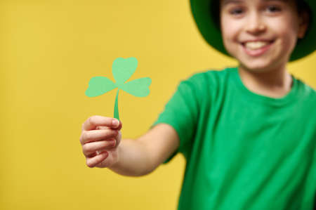 Focus on child's hand holding a clover leaf isolated on yellow background. Saint Patrick Dayの写真素材