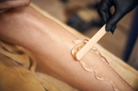 Closeup of woman's leg and aesthetician's hand applying a transparent gel with spatula before laser epilationの写真素材