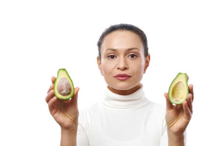 Confident portrait of young brunette woman with halves of avocado isolated on white background with...