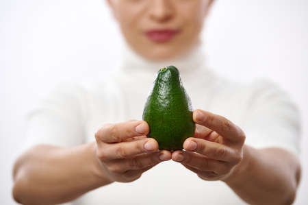 Closeup of woman's hands holding green avocado. Healthy eating, raw food diet. Vegetarian lifestyle. Proper nutrition.Copy space.の写真素材