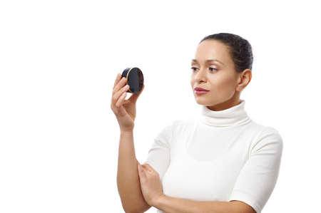 Young woman looks at a black container in her hand standing isolated on a white background with copy spaceの写真素材