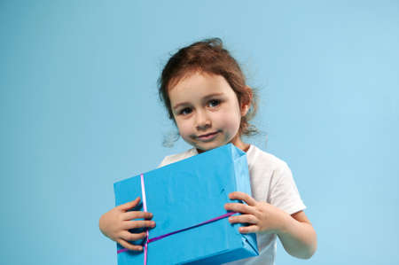 Adorable girl with blue gift on blue background. Copy space. Children Day. Birthday concept.の写真素材