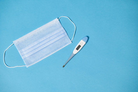 High angle view of protective medical mask and thermometer on blue background with copy spaceの写真素材