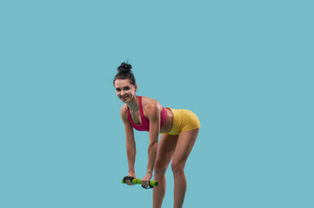 Sexy sportswoman exercising with dumbbells on blue background with copy space for promotion.