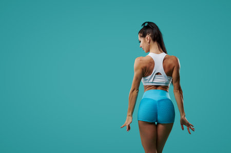 Pumped up fitness woman showing back and biceps muscle strength posing with her back to the camera...
