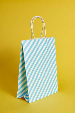 Paper gift bag in a blue white stripe on a yellow background, shot with a light shadow. A copy of the advertising spaceの写真素材