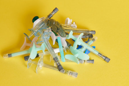 A tack of different syringes with beauty injections lying on yellow background with copy space. Shot with light shadow.の写真素材
