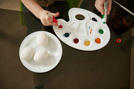 Close-up of a little boy's hand squeezing green paint from a tube onto a palette for coloring Easter eggsの写真素材