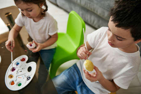 High angle view of two cute children decorating Easter eggs with color paints. Traditional Easter celebration conceptの写真素材