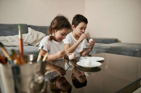 Two adorable children decorating Easter eggs at home. Traditional religious event.の写真素材