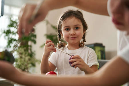 View through boy's hands to a cute smiling little girl with braids , looking at camera while...