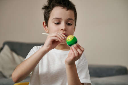 Adorable boy decorating Easter egg using paintbrush and paints.children's creativity Painting eggs