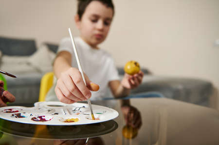 Closeup of a sckoolboy's hand holding a paintbrush and picking up a paint from color palette for decorating Easter eggの写真素材