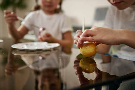 Closeup of hands of a boy holding a paintbrush and decorating an Easter egg with yellow gouache.の写真素材