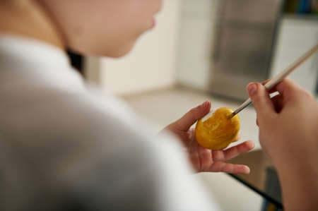 Closeup of hands holding a paintbrush and decorating an Easter egg with a yellow gouache for Easter. Traditional celebration conceptの写真素材