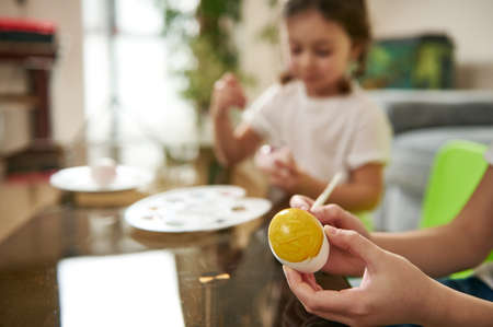 Closeup of an easter egg in the hand of a boy on the background of blurred girl decorating eggs for Easterの写真素材