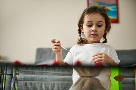 Beautiful preschool girl drawing and painting sitting at table at homeの写真素材