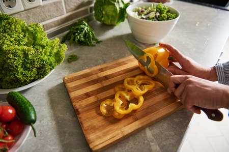 Female hands holding a knife and cutting yellow pepper into rings. High angle view. Closeup.の写真素材