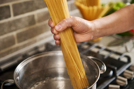 Close-up of female hands holding spaghetti and throwing them into boiled water.の写真素材