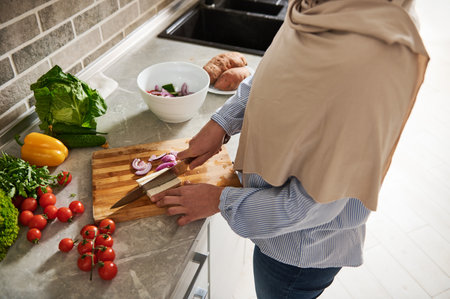 High angle view of a Muslim woman in hijab cutting tofu cheese and vegetables while preparing...