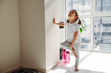 Beautiful little girl standing near a wall and learning performing tree pose in yoga. Proper healthy parenting, meditationの写真素材