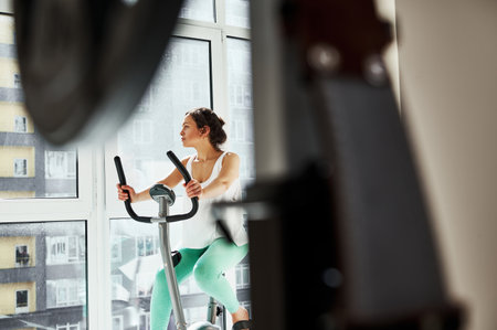 Beautiful woman looks towards the window while exercising on an exercise bike. Healthy habits...