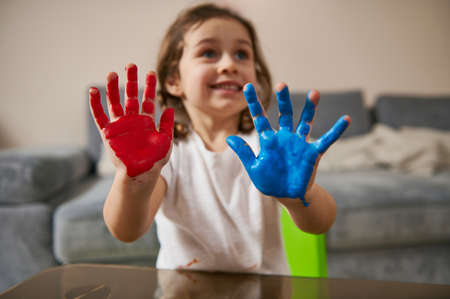 Focus on painted hands in blue and red paints of an adorable little girlの写真素材