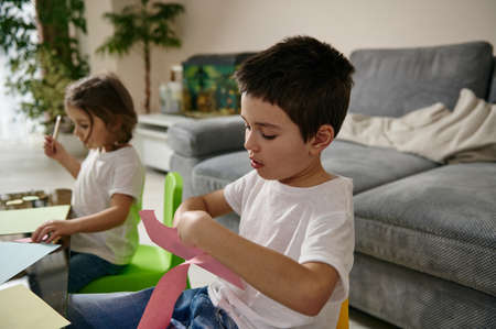 Schoolboy and preschool girl focused on creativity. Drawing and cutting shapes from color paper at home. Artの写真素材