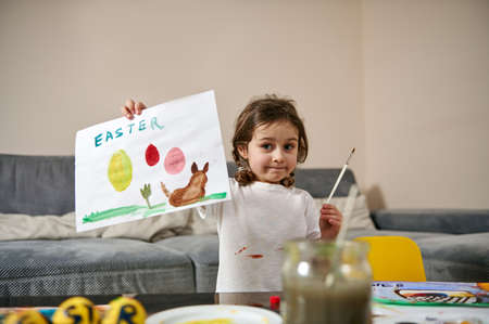 A happy little girl showing her beautiful drawing to the camera, Easter theme, watercolor technique. Children creative artの写真素材