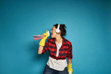 African American woman, housewife, with headphones holding cleaning sprays in her hands and singing with her eyes closed, enjoying her homework. Copy spaceの写真素材