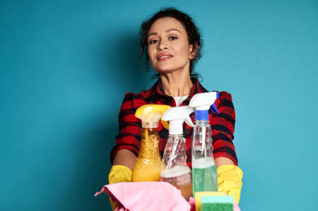 Beautiful young female cleaning contractor holding a tray with cleaning products. Cleaning concept. Blue background with copy spaceの写真素材