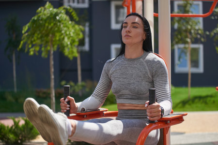 A young woman with flat belly shaking the press while raising her legs on the uneven bars. Front...