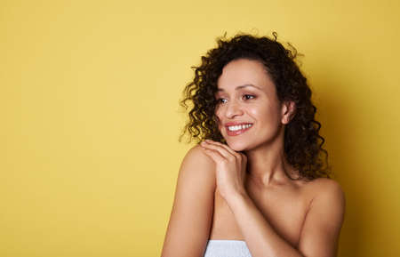 Attractive African American young woman with curly hair looking away and smiling with toothy smile....