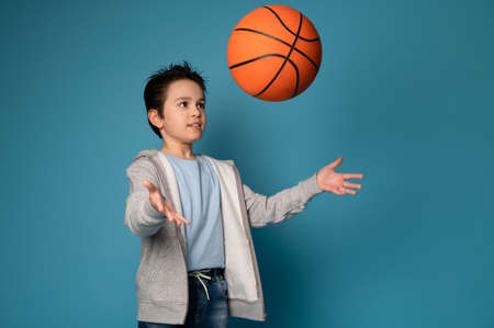 Adorable boy child throwing a ball while playing basketball. Isolated portrait of a young basketball...