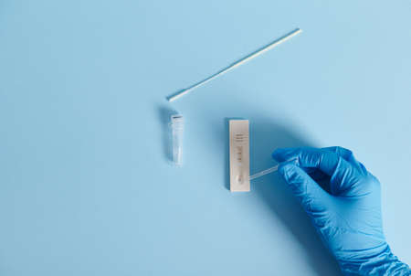 A hand in a protective medical glove drips a reagent into a test strip and makes a test for virus on...