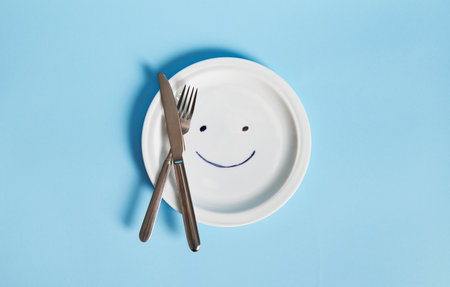 Cutlery on an empty plate painted with a smiley face, isolated on blue background with copy spaceの写真素材