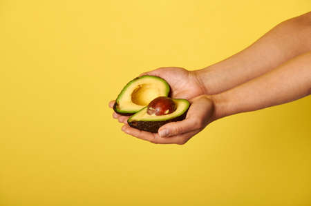 Closeup of hands holding two halves of ripe ready-to-eat avocado. Closeup on yellow background with copy spaceの写真素材